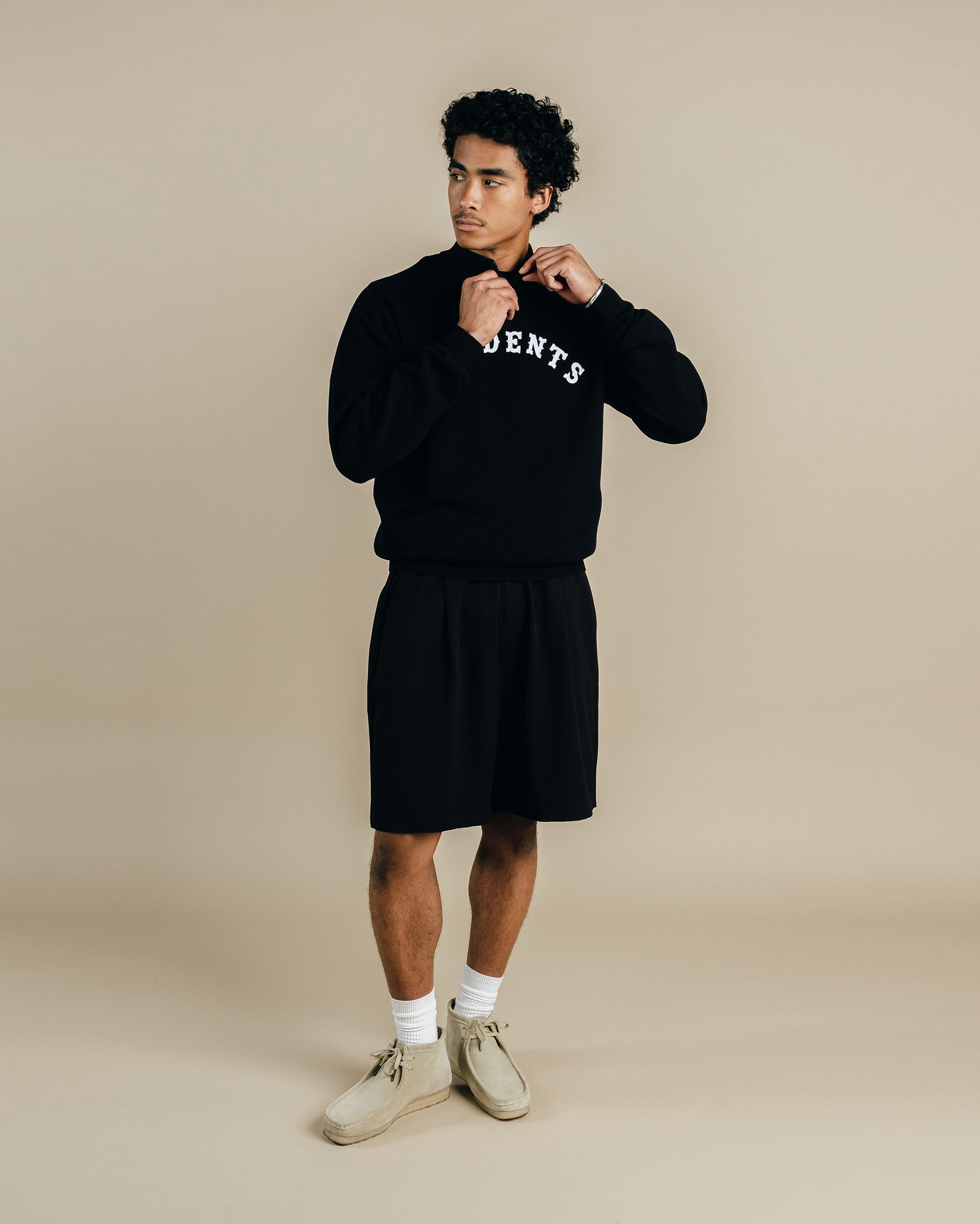 Man wearing a black sweatshirt with text and shorts on a beige background