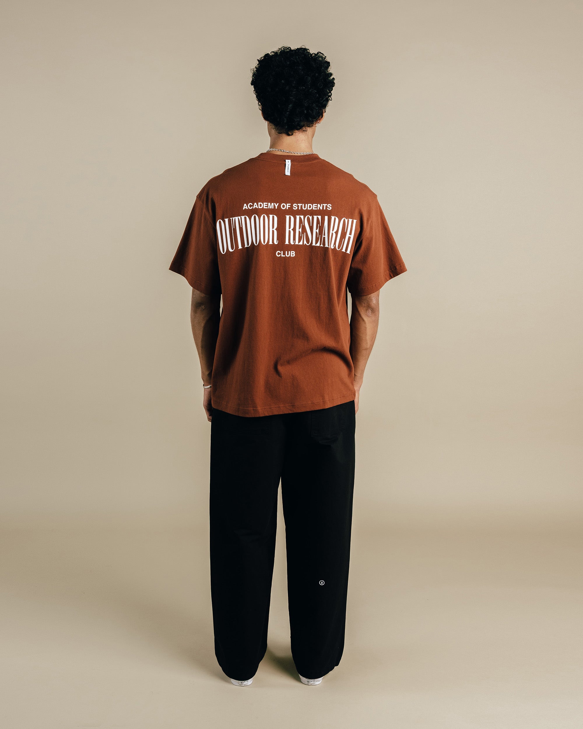 Person wearing a brown 'Outdoor Research' t-shirt on a beige background