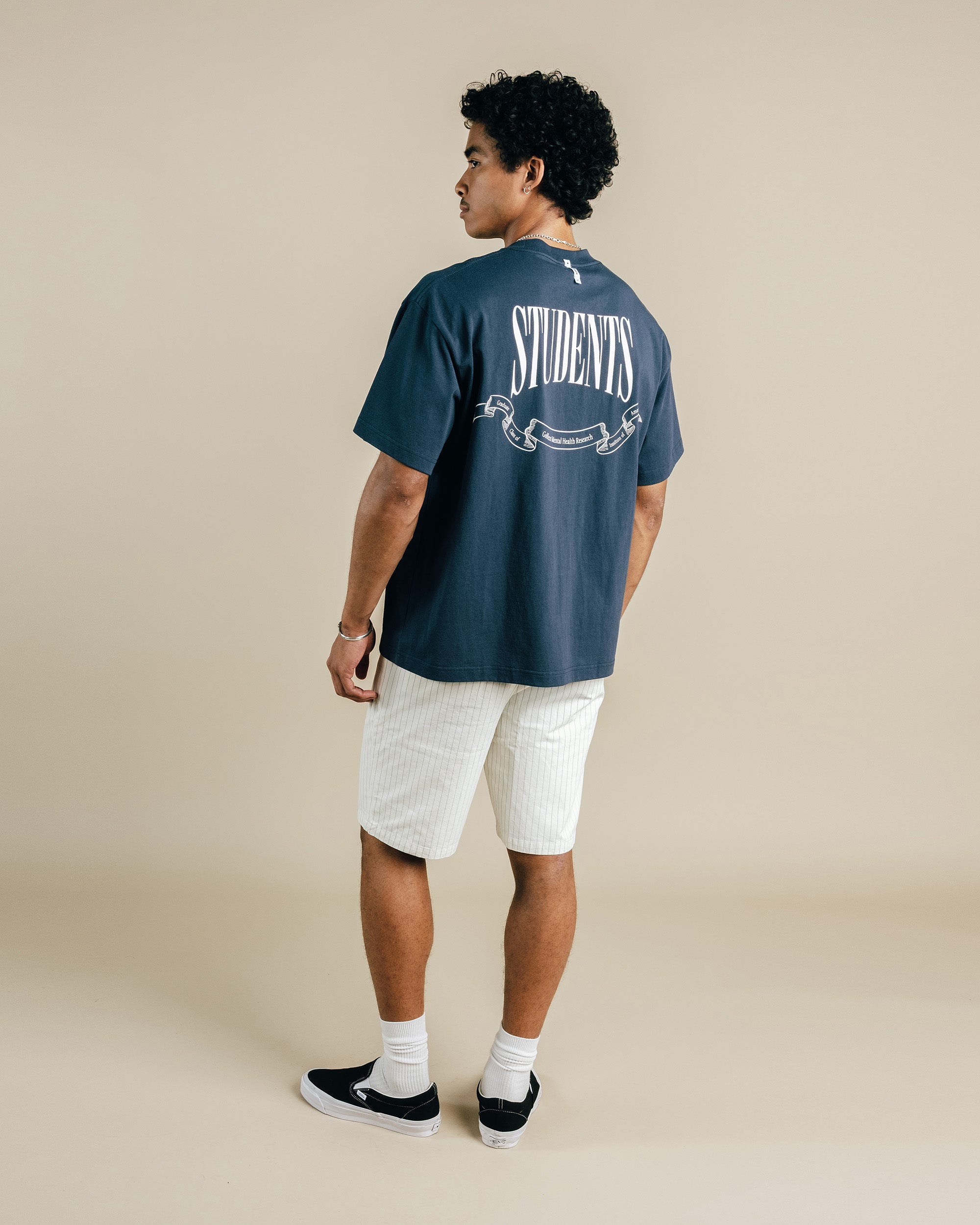 Person wearing a blue t-shirt with 'STUDENTS' printed on the back, standing against a beige background.