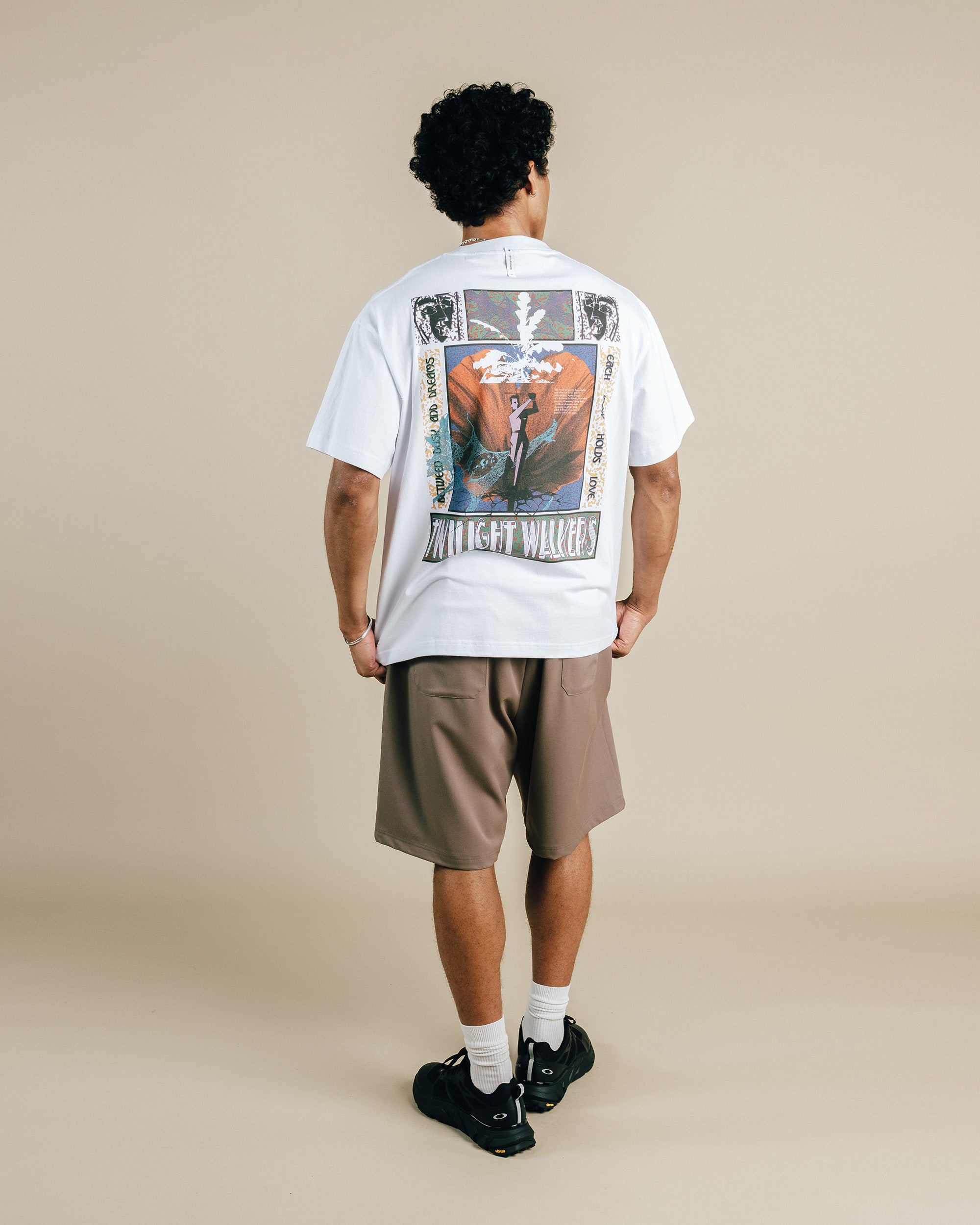 Person wearing a white t-shirt with a graphic design on the back, standing against a beige background