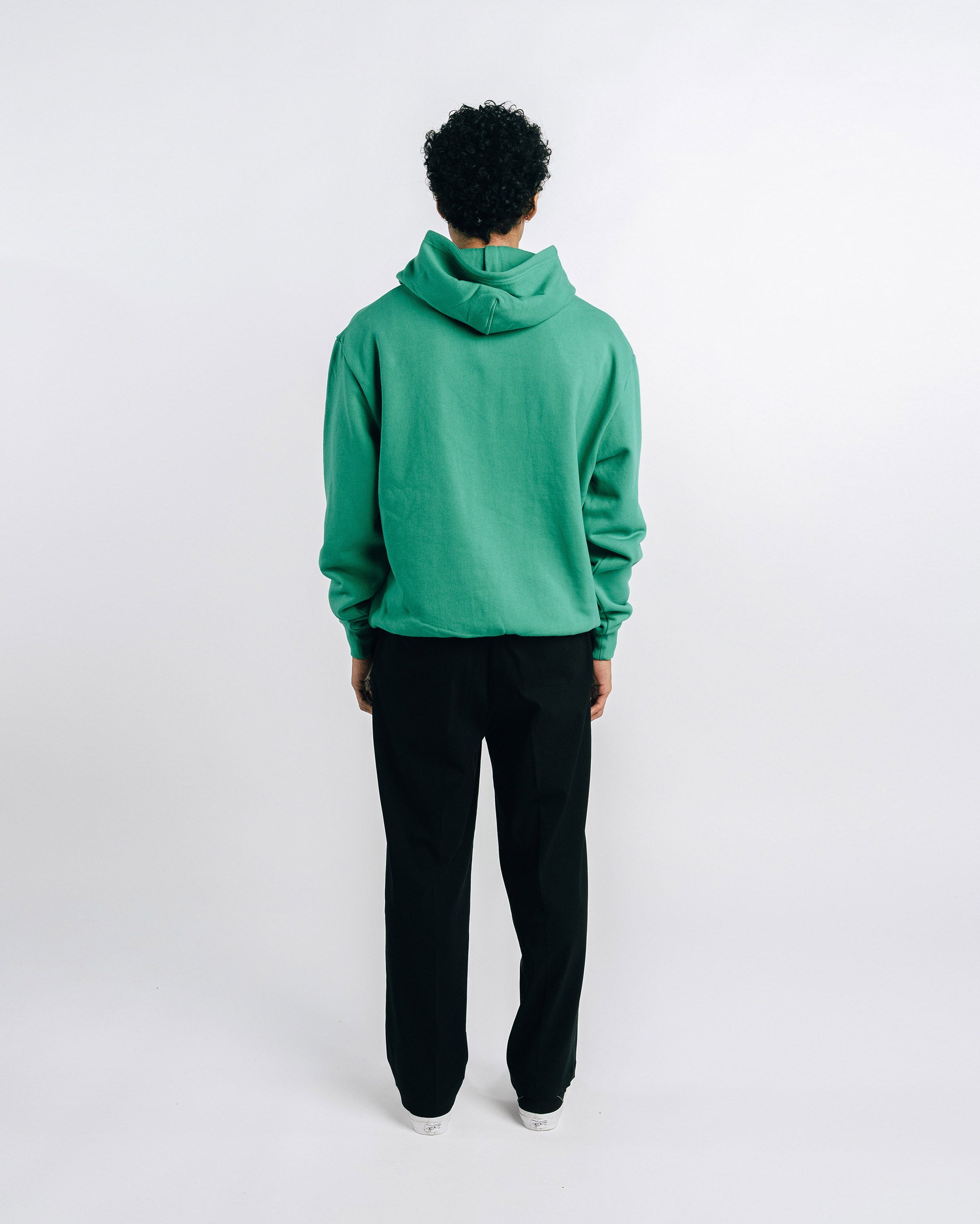 Person wearing a green hoodie and black pants on a white background
