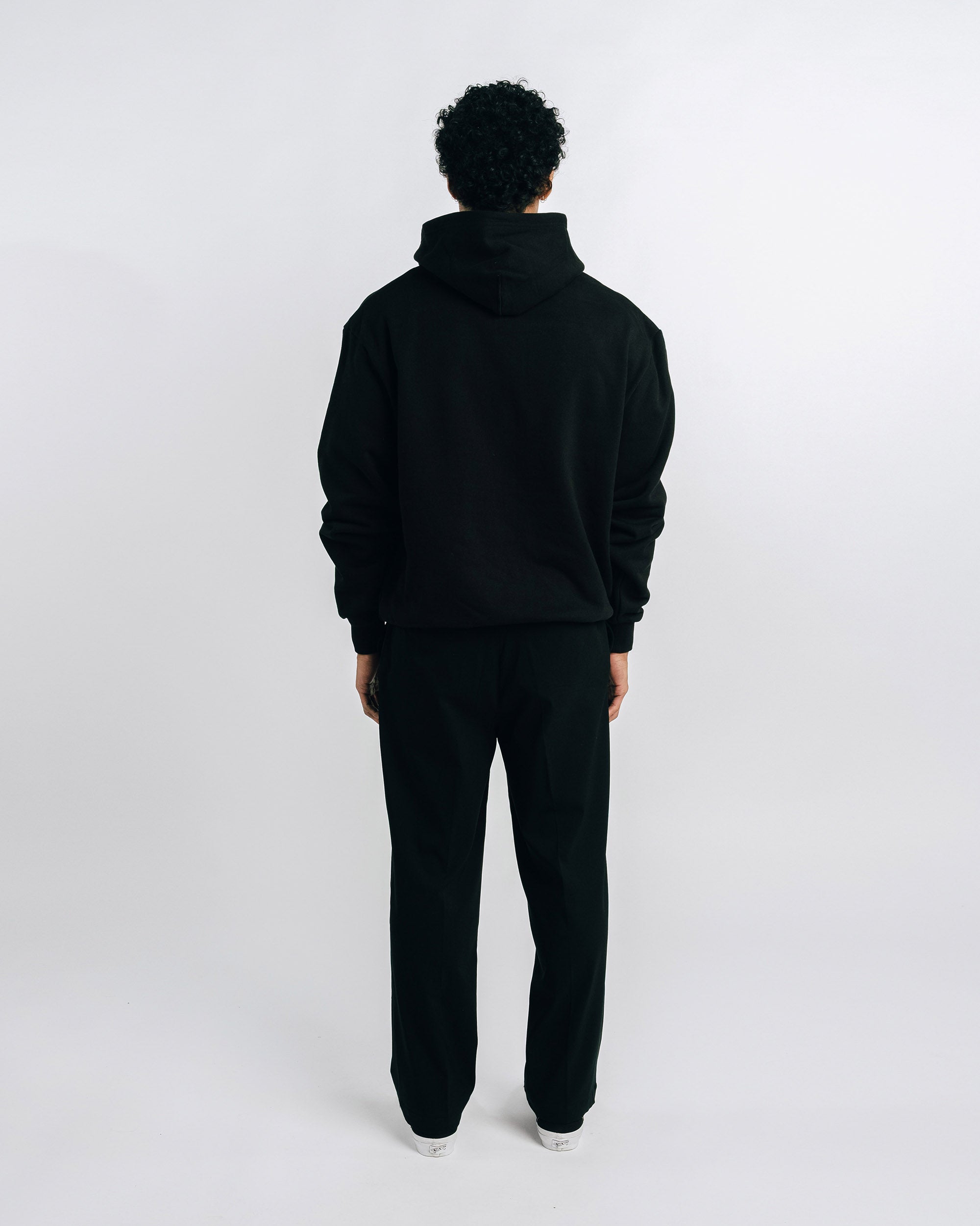 Person wearing a black hoodie and pants on a white background