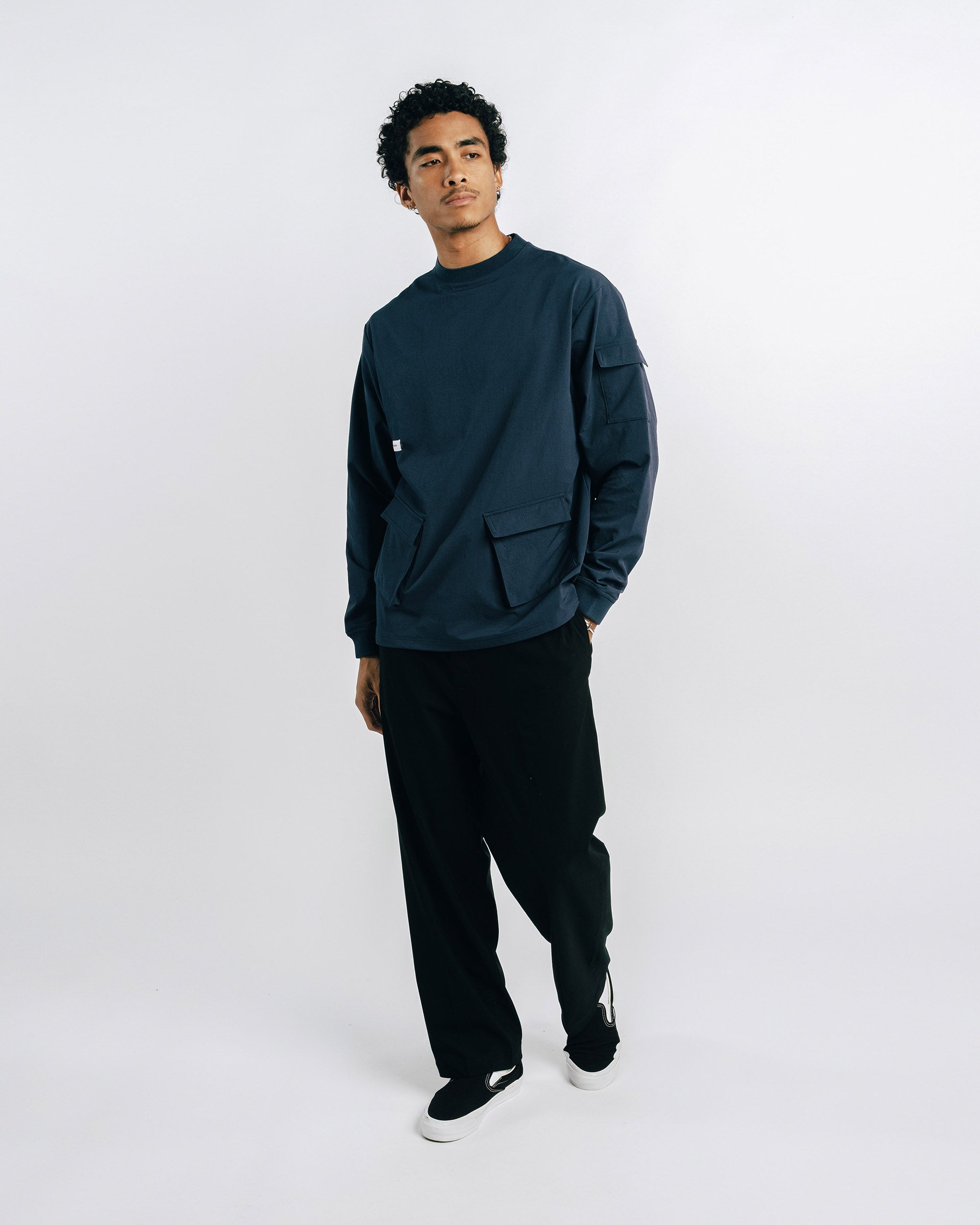 Man wearing a dark green sweater and black pants on a white background