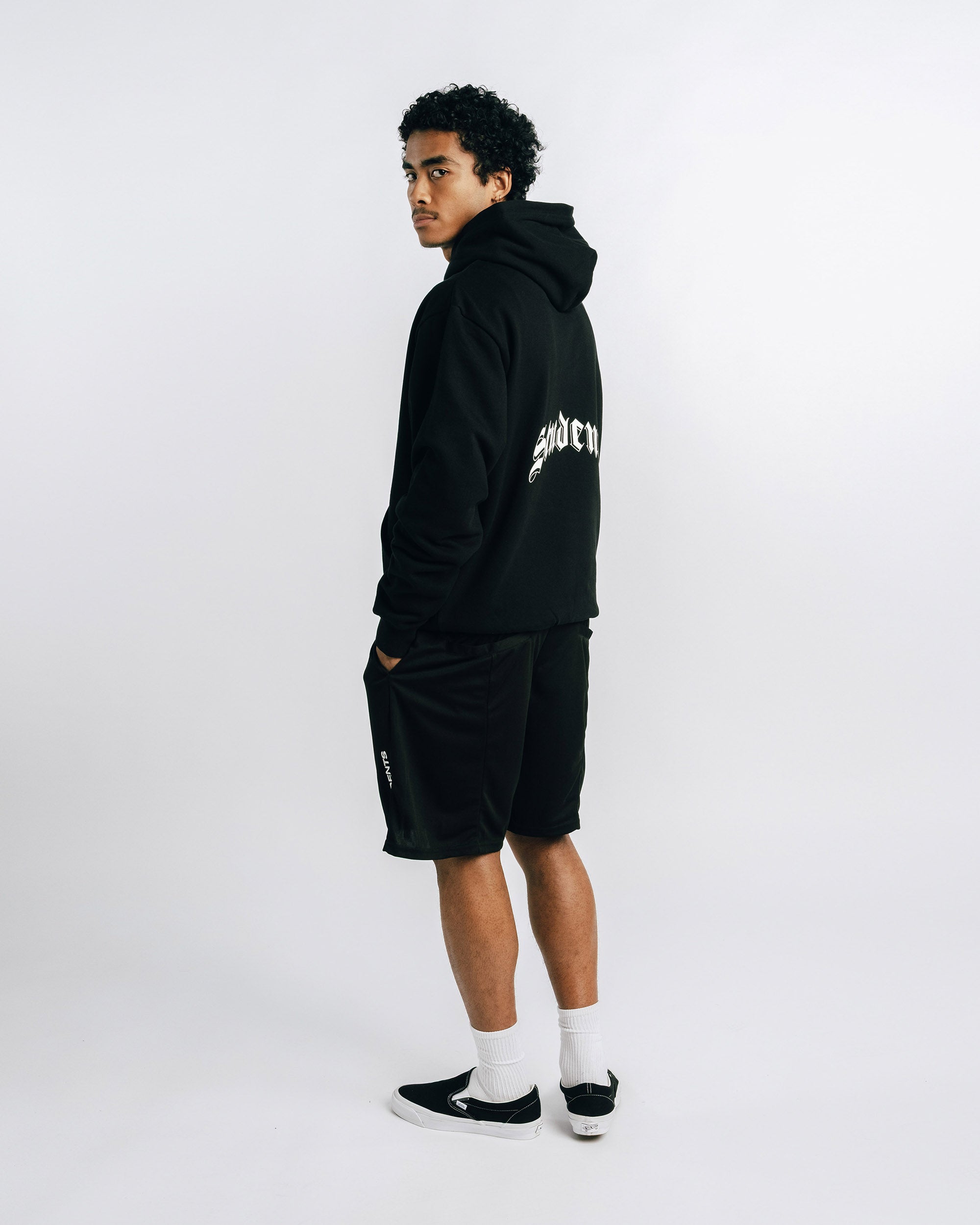 Person wearing a black hoodie and shorts with visible branding on a white background